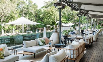 a modern outdoor living area with multiple couches and chairs , surrounded by lush greenery and trees at Crystalbrook Byron