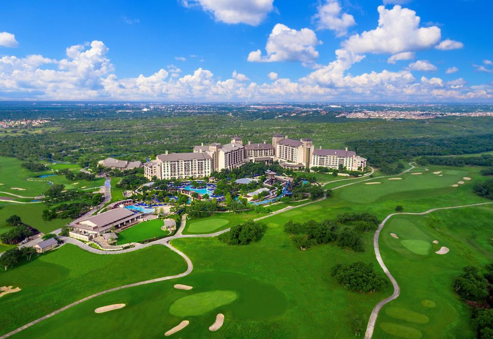 a bird 's eye view of a large hotel surrounded by green grass and trees , with a golf course in the foreground at JW Marriott San Antonio Hill Country Resort & Spa