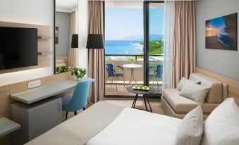 a hotel room with a bed , couch , and balcony view of the ocean , as well as a desk and chairs at Valamar Meteor Hotel