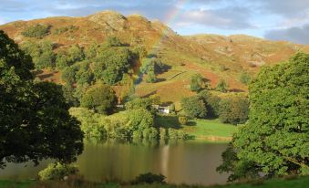 a picturesque mountain landscape with a lake surrounded by green hills , and a rainbow in the sky at The Punchbowl Hotel