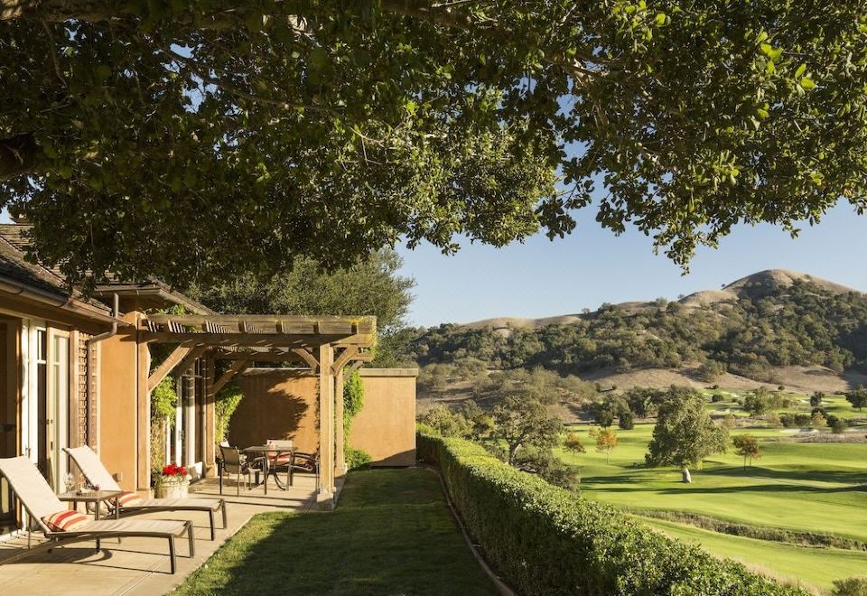 a wooden pergola is surrounded by a garden and has chairs on the deck , overlooking a golf course at CordeValle