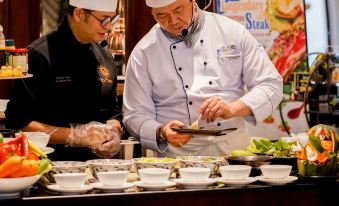 two men wearing chef 's hats are preparing food in a restaurant kitchen , preparing a meal together at Alagon Saigon Hotel & Spa