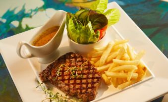 a plate of food , consisting of steak , fries , and salad , placed on a dining table at Garden Hotel