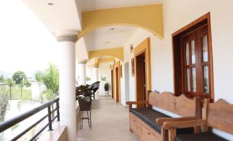 a long , covered walkway with wooden benches and a balcony , leading to a building with yellow and white walls at Hotel Restaurante Donaji