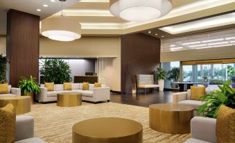 a modern lounge area with white and gold furniture , surrounded by large windows and potted plants at Hilton Melbourne, FL