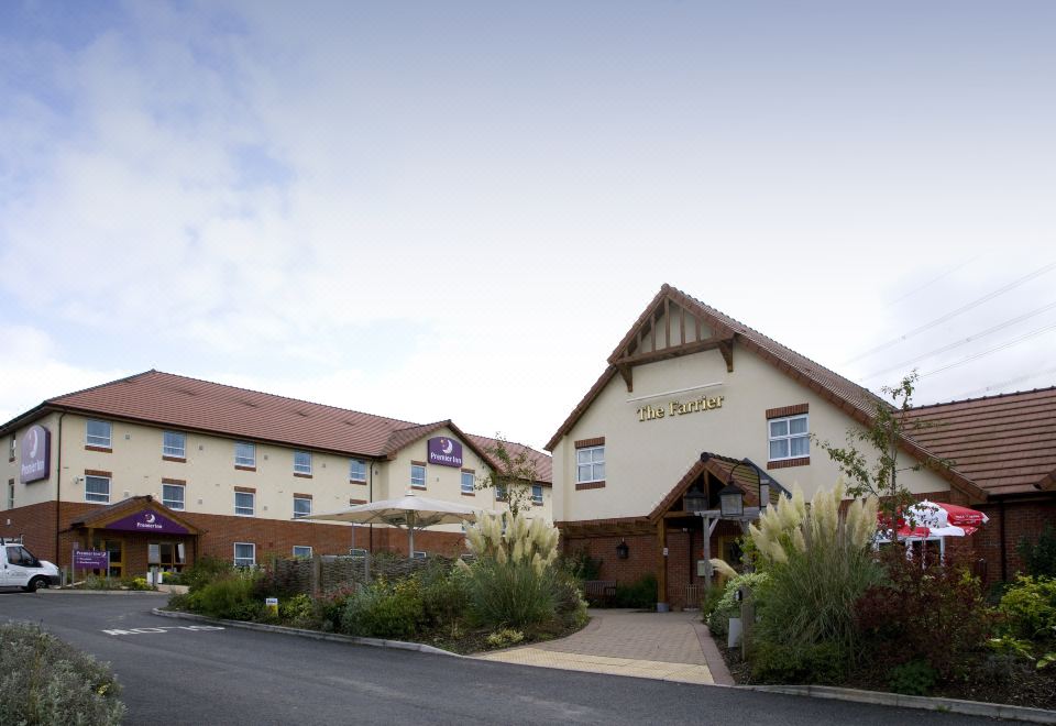 a large hotel building with a red roof , surrounded by grass and trees , under a clear blue sky at Premier Inn Grantham