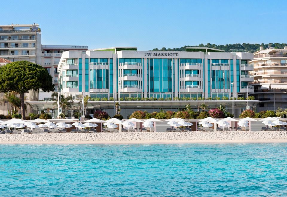 a large building on the beach , surrounded by chairs and umbrellas , creating a relaxing atmosphere at JW Marriott Cannes