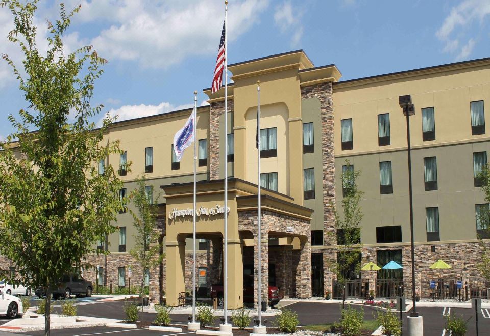 a large hotel building with multiple flags flying in front of it , and a parking lot nearby at Hampton Inn & Suites by Hilton Stroudsburg Pocono Mountains