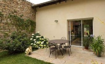 a backyard with a small patio set , flowers , and a sliding glass door leading to an outdoor dining area at Le Cercle Chambres climatisées