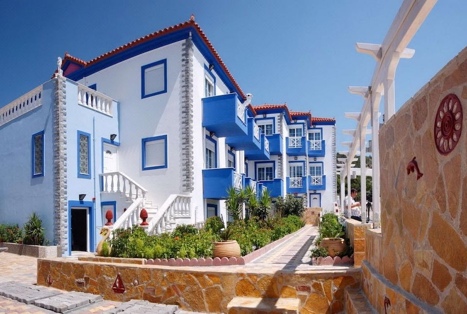 a blue and white building with red tile roof , surrounded by plants and a stone walkway at Aphrodite Beach Hotel