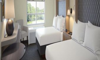 a hotel room with two beds , each made up with white sheets and pillows , next to a window that offers a view of trees outside at Holiday Inn & Suites Arden - Asheville Airport