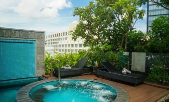 a hot tub is surrounded by lounge chairs and greenery , with a large building in the background at Alagon Saigon Hotel & Spa