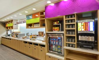 a colorful breakfast nook with a variety of food and drinks , including cereal , juice , and other snacks at Home2 Suites by Hilton Helena