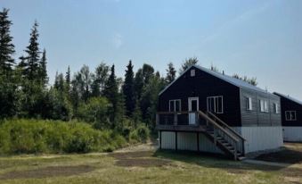 a black house with a wooden deck and stairs is surrounded by tall trees in a forested area at The Cannery Lodge