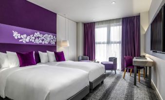 a hotel room with two beds , a chair , and a window , decorated with purple walls and curtains at Mercure Hai Phong