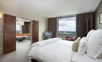 a large bed with white linens is situated in a room with a window and couch at Pullman at Sydney Olympic Park