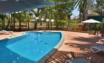 a backyard with a swimming pool surrounded by chairs and umbrellas , creating a relaxing atmosphere at Parry Creek Farm Tourist Resort & Caravan Park