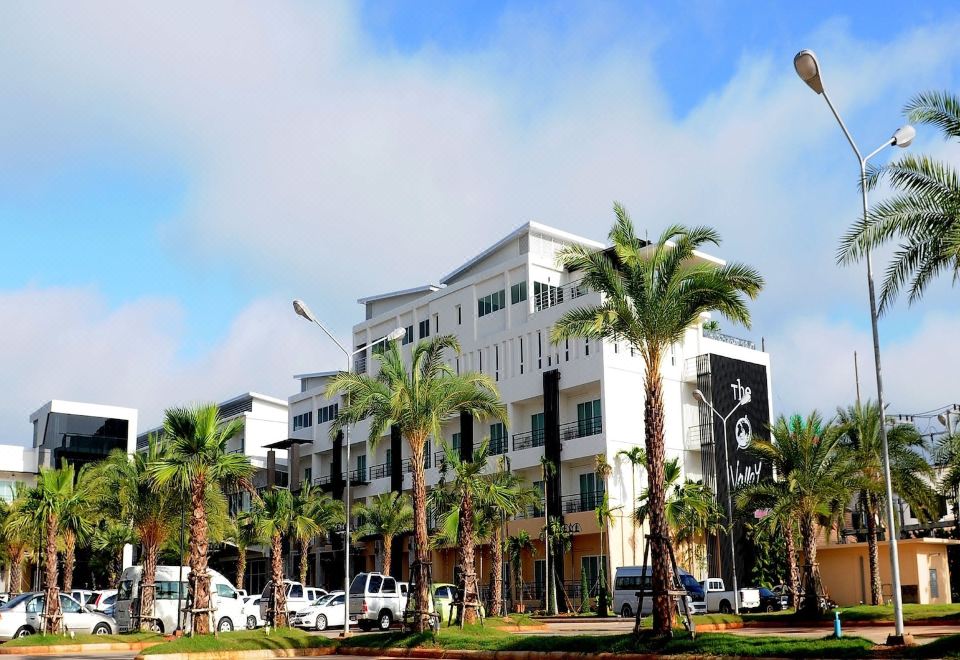 a modern white building with palm trees in front , surrounded by a parking lot filled with cars at The O Valley Hotel