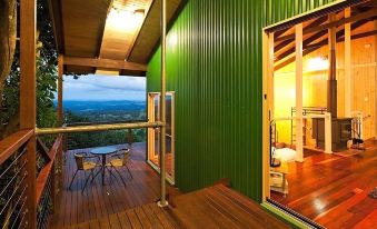a green cabin with a balcony overlooking a beautiful view , complete with a dining table and chairs at Treetops Montville