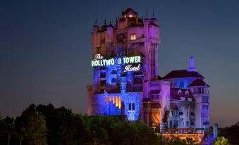 a large , ornate hollywood tower hotel with its sign illuminated at night , set against a dark background at Disney's All-Star Sports Resort