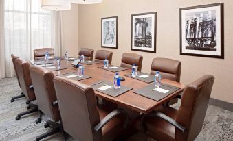 a conference room with a wooden table , brown chairs , and framed pictures on the wall at Courtyard Houma