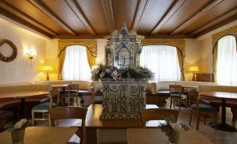a dining room with wooden tables and chairs , a large vase in the center of the room , and yellow curtains on the windows at Grand Hotel Misurina