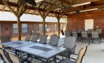 a large wooden dining table surrounded by chairs under a covered area , with a ceiling fan hanging from the ceiling at New Hochatown Lodge