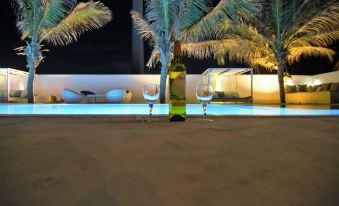 a bottle of wine and two glasses are placed on the edge of a pool , surrounded by palm trees at Dolphin Beach Resort