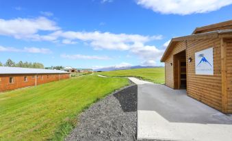 a house with a driveway leading to it , surrounded by green grass and mountains in the background at Hotel Eyjafjallajokull