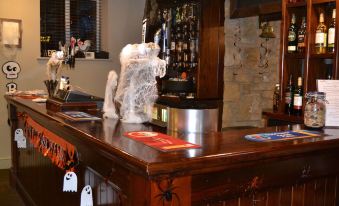 a bar with a wooden counter , two bottles of liquor on the counter , and halloween decorations at Anglers Arms