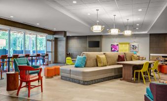 a modern hotel lobby with various seating options , including couches and chairs , under hanging lights at Home2 Suites by Hilton Fort Mill