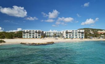 a large , modern apartment building situated on the edge of a body of water , surrounded by trees and clouds at Curacao Marriott Beach Resort