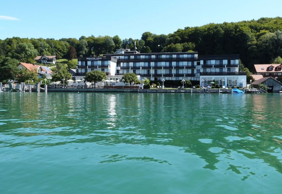 a large hotel is situated on the shore of a body of water , surrounded by trees at Seehotel Leoni