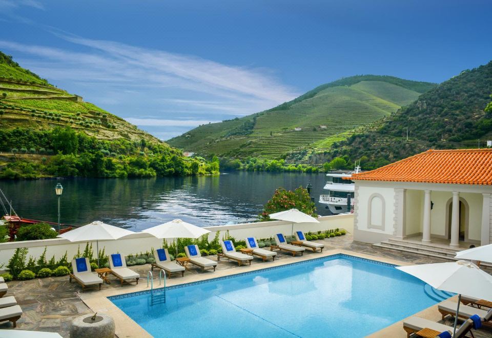 a beautiful swimming pool with sun loungers and umbrellas , overlooking a serene lake and mountains under a clear blue sky at The Vintage House - Douro