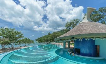 a large blue pool with a thatched roof structure is surrounded by trees and water at Island Escape by Burasari