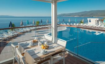 a balcony overlooking a pool and the ocean , with a table and chairs set up for dining at Valamar Bellevue Resort