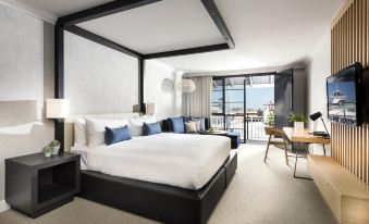 a modern hotel room with a large bed , white bedding , and a balcony offering views of the city at Tradewinds Hotel and Suites Fremantle