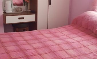 a pink bedspread on a white comforter , with a wooden wardrobe and drawers in the background at Gracelands Guest House