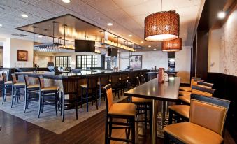 a modern restaurant with a long wooden table and multiple chairs , along with a bar area at Wyndham Minneapolis South/Burnsville