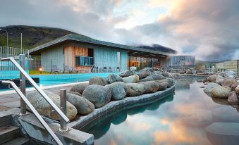 a large outdoor pool surrounded by a stone wall , with a building in the background at Hotel Selfoss