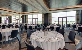 a large dining room with numerous round tables covered in white tablecloths , set for a formal event at Hilton Garden Inn Doncaster Racecourse