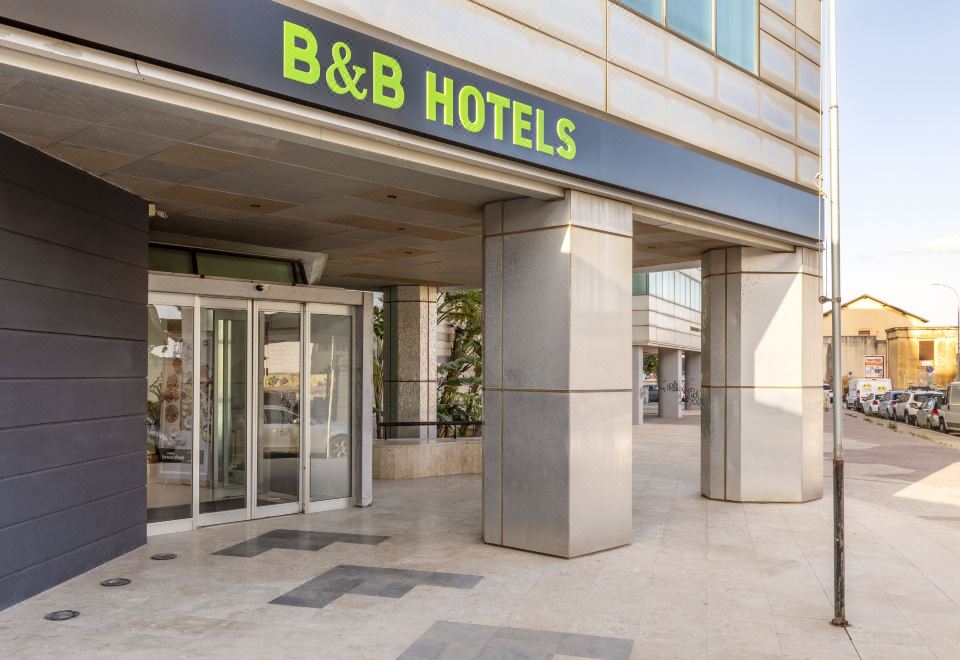 a modern building with a b & b hotels sign on the entrance , and a concrete walkway leading up to the entrance at B&B Hotel Trapani Crystal