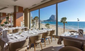 a restaurant with white tables and chairs is set up in front of a large window overlooking the ocean at Solymar Gran Hotel
