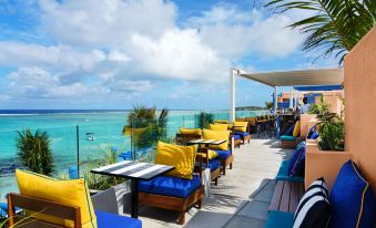 a rooftop terrace with blue and yellow cushions , wooden tables , chairs , and a view of the ocean at Salt of Palmar, Mauritius, a Member of Design Hotels