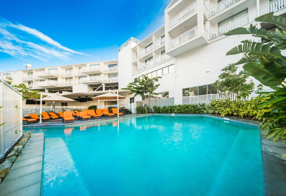 a large swimming pool is surrounded by orange lounge chairs and a white building with balconies at Airlie Beach Hotel