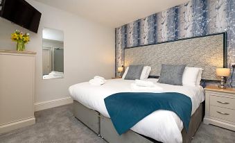 a large bed with a blue blanket and white pillows is in a room with gray carpeting at Portbyhan Hotel
