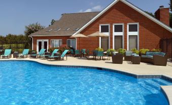 a large swimming pool surrounded by lounge chairs and umbrellas , with a house in the background at Suites Birmingham