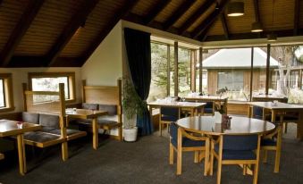 a dining area with wooden tables and chairs , surrounded by windows that offer a view of the outdoors at Alpine Lodge