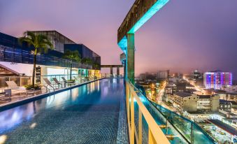 a large , modern rooftop pool with a balcony overlooking the city at night , illuminated by colorful lights at Cosmos Pacifico Hotel