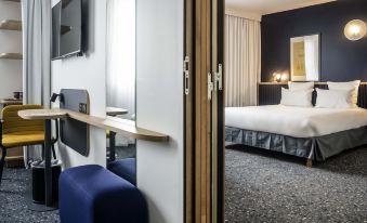 a hotel room with a blue chair , white bed , and an open door leading to the bathroom at Ibis Styles Paris Romainville